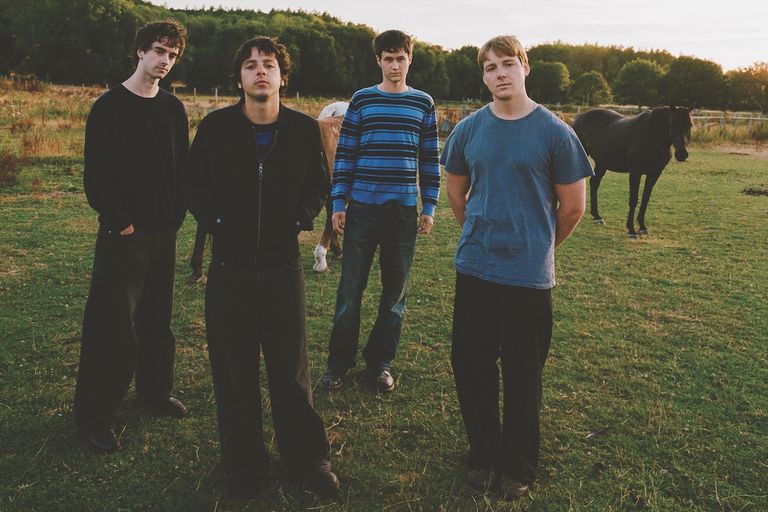 Australian band Radio Free Alice posing outdoors in a grassy field with horses, shot by Imogene Barron.